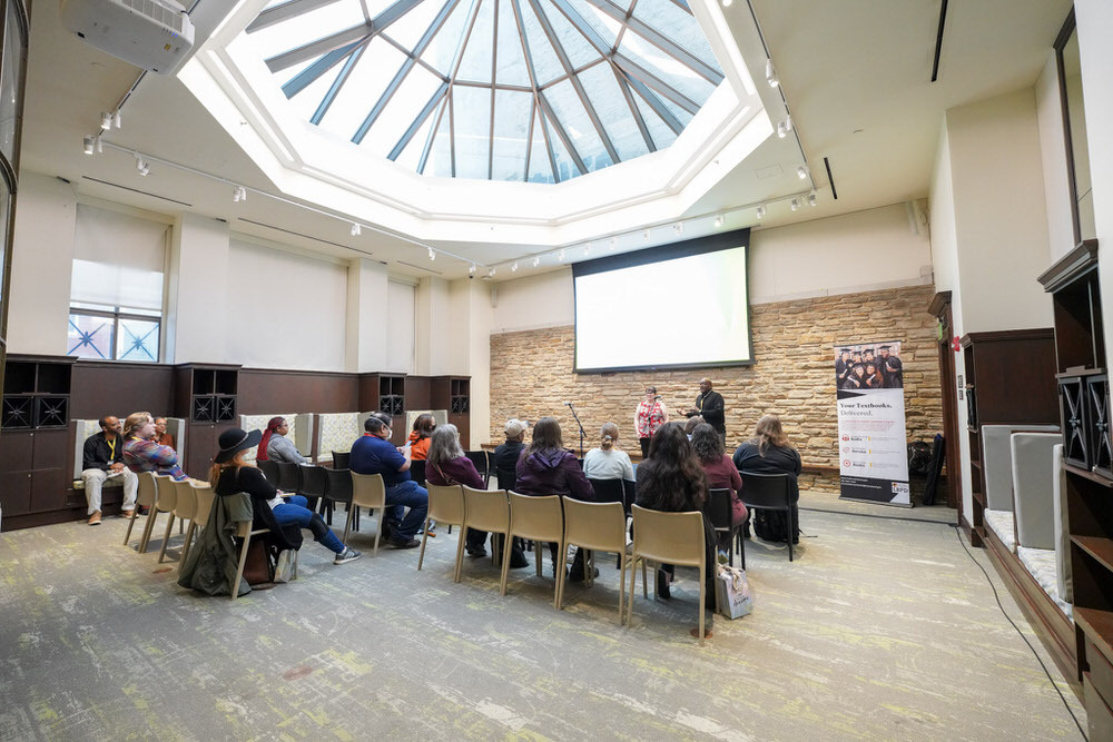 photo from a SLRC conference showing people speaking, a seated audience, and screen in the Central Library's Sun Room