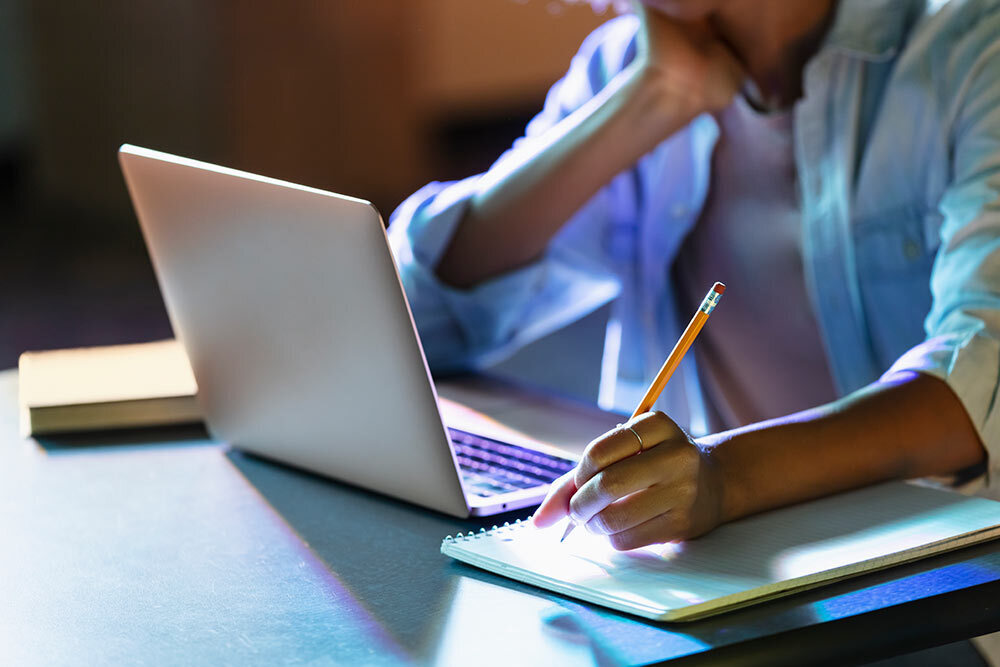 research - a person taking notes with a laptop and pen in blue light